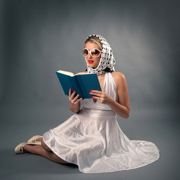 Retro woman with sunglasses reading book portrait against dark background. - Photo, image