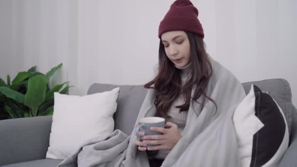 Beautiful attractive Asian woman holding a warm cup of coffee or tea while lying on couch when relax in her living room at home. Lifestyle women at home in Christmas and New year holidays concept. - Filmati, video