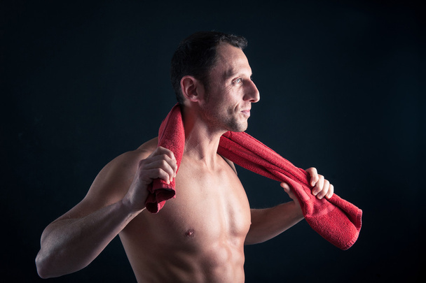 Confident young man shirtless portrait with red towel against black background. - Photo, Image