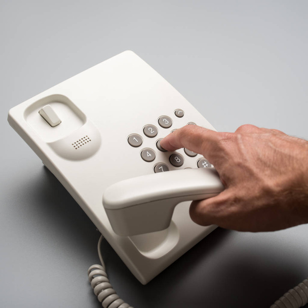 Męskiej ręki wybierania numeru telefonicznego przy użyciu telefonu stacjonarnego białe, szare tło. - Zdjęcie, obraz