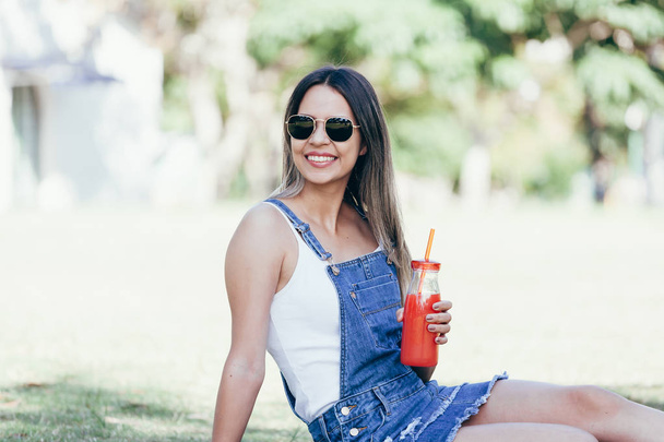 Portrait of a beautiful young woman, drinking juice on a sunny day in the park - Photo, Image