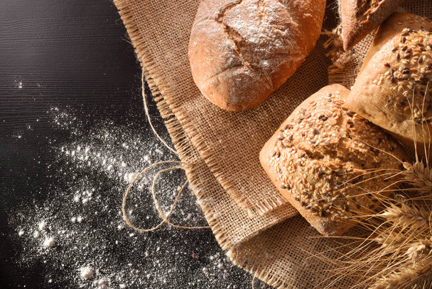 Assortment of bread on sackcloth and flour on black table. Top view. Horizontal composition - Foto, afbeelding