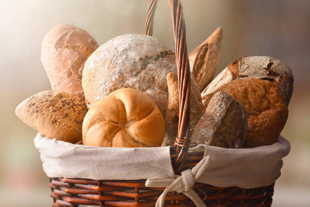 Assortment of breads over a wicker basket in a rustic kitchen. Horizontal composition. Front view - Φωτογραφία, εικόνα