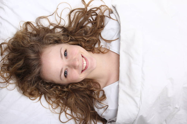 Beautiful young girl is lying on bed and smiling - Foto, Bild