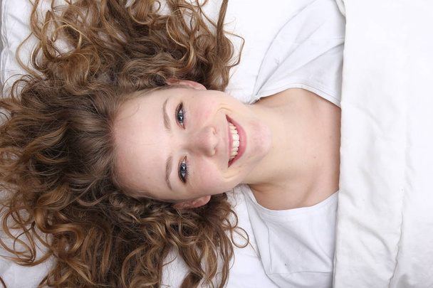 Mooi jong meisje is liggend op bed en glimlachen - Foto, afbeelding