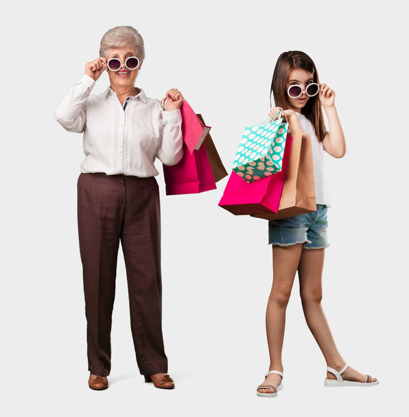 Corpo pieno di una signora anziana e sua nipote allegra e sorridente, molto eccitata portando una shopping bag, pronta per andare a fare shopping e cercare nuove offerte
 - Foto, immagini