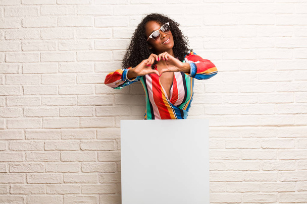 Fiatal fekete nő, így egy szív kezek ellen tégla fal fehér lobogóval - Fotó, kép