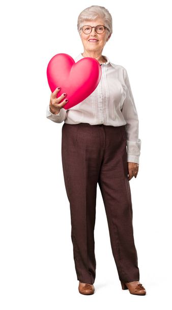 Mujer mayor de cuerpo completo alegre y confiada, ofreciendo una forma de corazón hacia el frente, concepto de amor, compañía y amistad
 - Foto, imagen