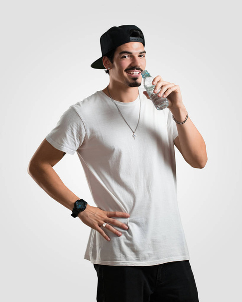 若いラッパー男が笑みを浮かべて満足、冷たい水の瓶を持って、その水和反応は体にとって重要な記憶 - 写真・画像