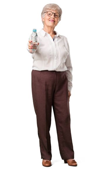 Ganzkörper-Seniorin lächelt zufrieden, hält eine Flasche kalten Wassers in der Hand und erinnert sich, dass Flüssigkeit wichtig für den Körper ist - Foto, Bild