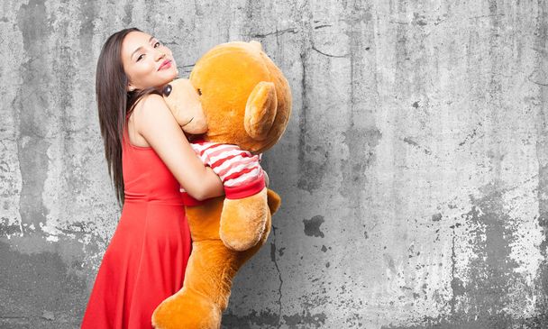 asian woman in red dress holding a teddy bear against grey grunge background - Фото, изображение