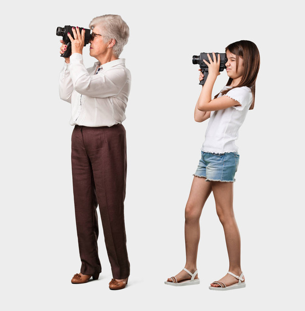 Cuerpo completo de una anciana y su nieta emocionadas y entretenidas, mirando a través de una cámara de cine, buscando una toma interesante, grabando una película, productor ejecutivo
 - Foto, Imagen
