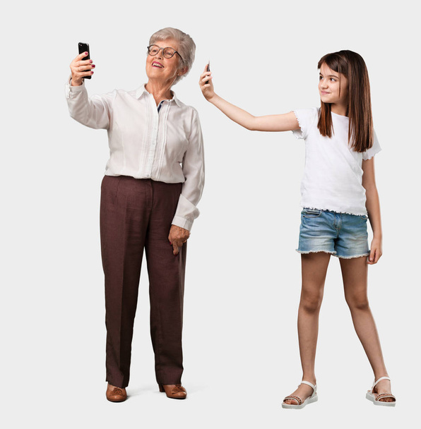 Teljes test és egy idős néni unokája magabiztos és vidám, figyelembe véve a selfie, néztem a mobil egy vicces és gondtalan gesztus, a társadalmi hálózatok és internet szörfözés - Fotó, kép