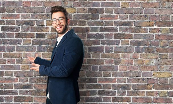 young man doing a welcome gesture against brick wall - Photo, Image