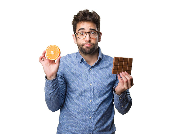 joven sosteniendo una naranja y una barra de chocolate aislada sobre fondo blanco
 - Foto, Imagen