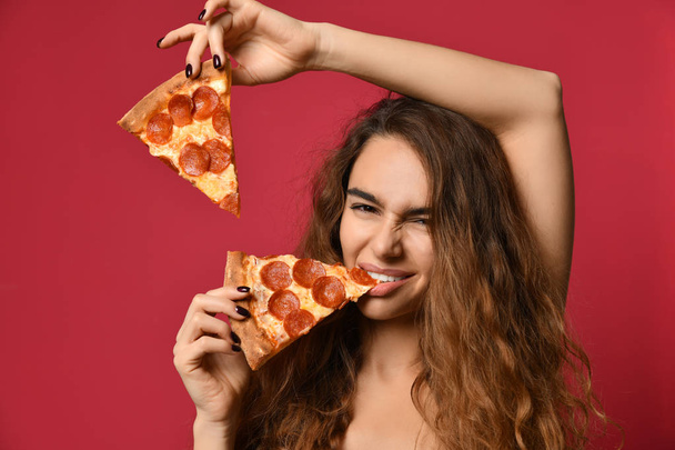 Young beautiful woman eating slice of pepperoni pizza on pink red - Foto, afbeelding
