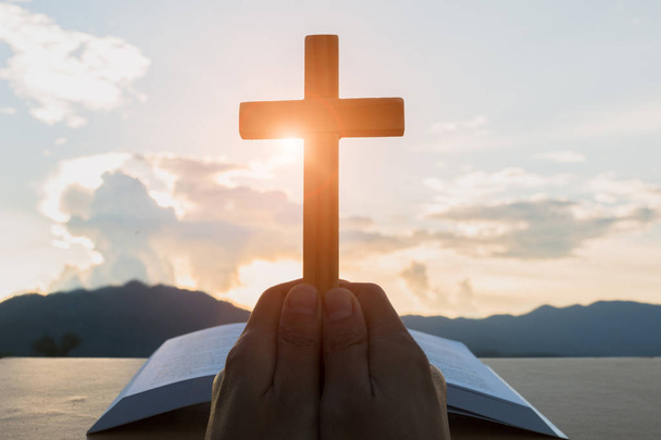 Hände mit Holzkreuz über offener russischer Bibel auf Sonnenaufgangshintergrund, Kruzifix, Symbol des Glaubens. - Foto, Bild