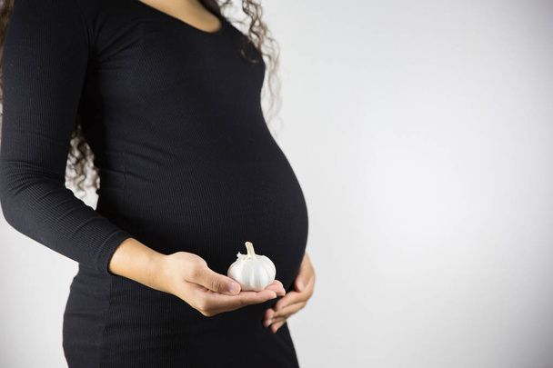 Η κατανάλωση σκόρδου κατά τη διάρκεια της εγκυμοσύνης. Υγιεινό φαγητό και έννοια. Έγκυος γυναίκα τρώει σκόρδο. - Φωτογραφία, εικόνα