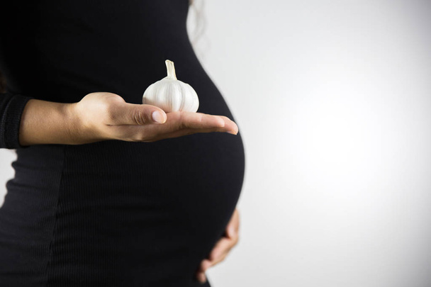 De consumptie van knoflook tijdens de zwangerschap. Gezond eten en mensen concept. Zwangere vrouw eten knoflook. - Foto, afbeelding