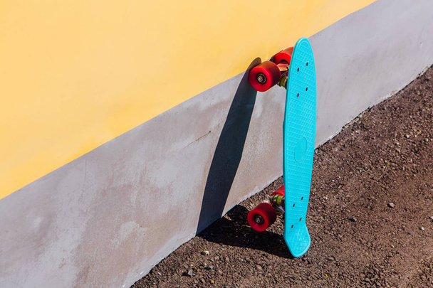 Blue plastic skateboard penny board with pink wheels stands next to the wall. - Foto, imagen