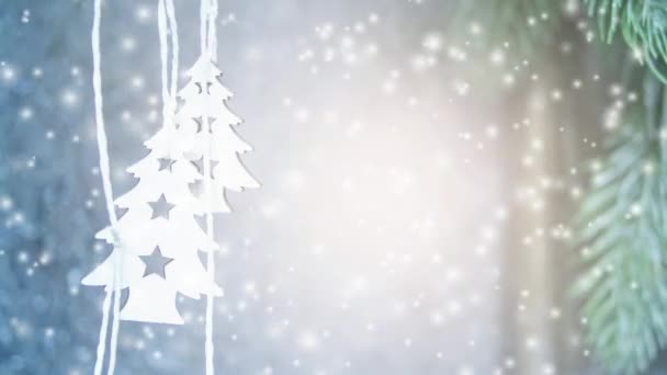 Kaksi pientä valkoista joulukuusta roikkuu harmaan seinän taustalla
 - Materiaali, video