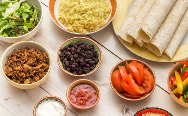 Ingredients to make mexican burritos with tortillas, rice, beans, ground beef, tomato, salsa, lettuce - Photo, Image