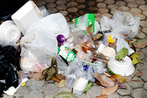hromadu plastových odpadků na podlaze, nesmyslné plastové odpadní sklo a brčka, plastového sáčku odpad, koše pěny zásobník na potraviny a suché listí - Fotografie, Obrázek