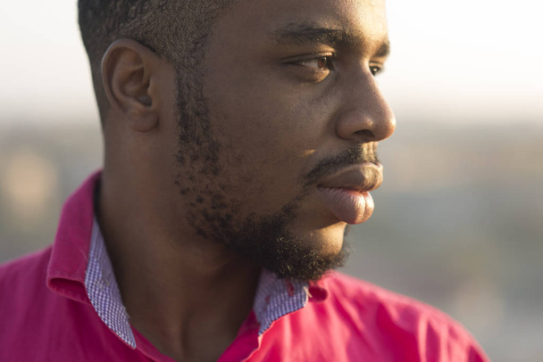 Man with beard and mustache at sunset, urban background, defocused. Man on calm relaxed face, close up. African peoples beauty concept. Macho with beard and smooth brown skin looks handsome - Valokuva, kuva