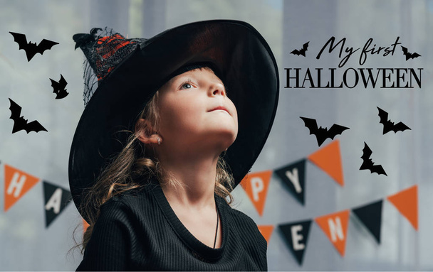 portret urocze dziecko w witch halloween kostium, odwracając się w domu z "mój pierwszy halloween" napis - Zdjęcie, obraz