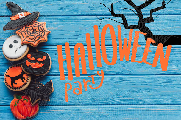 bovenaanzicht van spooky zelfgemaakte halloween cookies geplaatst in rij op blauwe houten achtergrond met "halloween party" belettering - Foto, afbeelding
