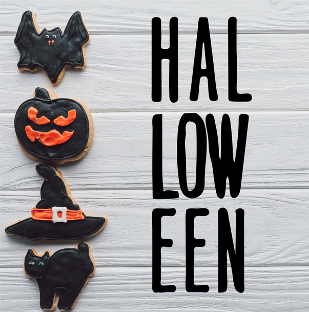 vista elevada de galletas de halloween caseras colocadas en fila sobre fondo de madera blanca con letras de "halloween"
 - Foto, Imagen