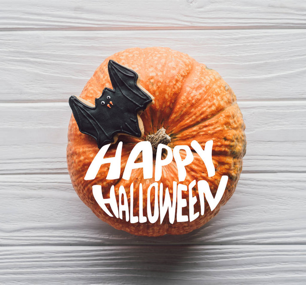 elevated view of pumpkin with homemade halloween cookie on wooden table  with "happy halloween" lettering - Фото, зображення