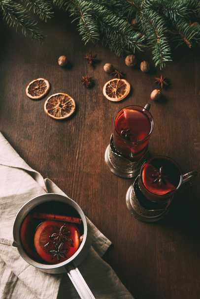 mulled wine in saucepan and glass cups on wooden background with dried orange slices and spices  - Photo, Image