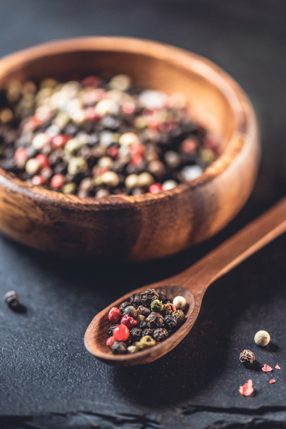 close-p view of wooden spoon and bowl with dried aromatic peppercorns on black - Photo, Image