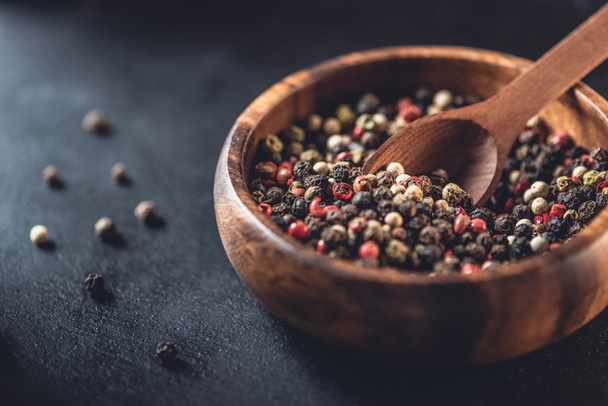 close-up view of wooden bowl and spoon with dried aromatic peppercorns on black - Foto, afbeelding