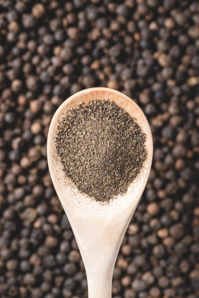 close-up view of wooden spoon with powdered pepper and peppercorns - Foto, imagen
