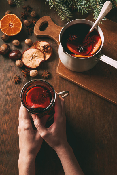 cropped view of woman holding glass of mulled wine on wooden background - Photo, Image
