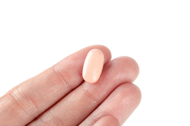 pill on fingers of female hand on white - Foto, afbeelding