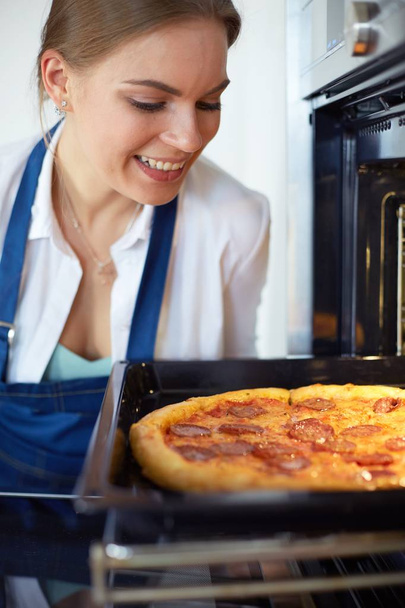 Happy young woman cooking pizza at home - Fotó, kép