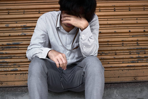 Vorderseite des traurigen depressiven jungen asiatischen Geschäftsmannes, der das Gesicht mit den Händen bedeckt. - Foto, Bild