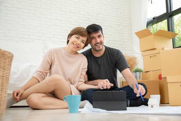 Gelukkige jonge paar met digitale tablet planning van hun nieuwe bewegende huis. Glimlachen elkaar. Op zoek naar camera. - Foto, afbeelding