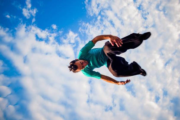 Jovem praticando exercício de parkour abaixo do céu azul
 - Foto, Imagem