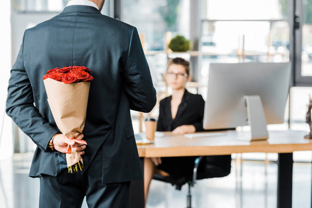 обрізане зображення бізнесмена, що ховає букет з троянд позаду, щоб здивувати бізнес-леді в офісі
 - Фото, зображення