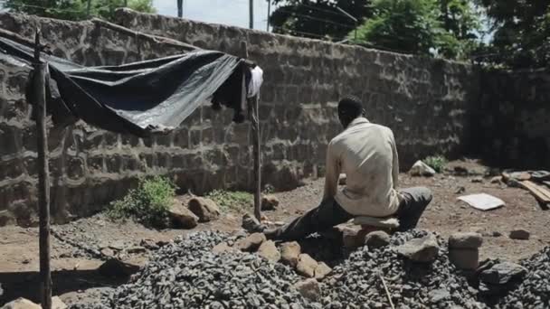 Adamın Afrika'dan arkadan görünüm inşaat alanında çalışır. Adam taş ocağının üzerinde oturuyor - Video, Çekim