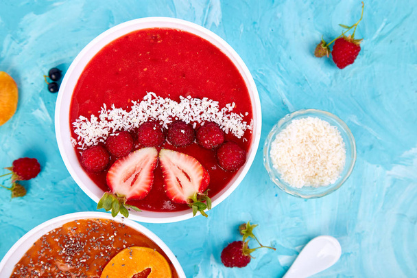 Smoothie bowls. Healthy breakfast bowl on blue background. Apricot smoothie with blackberry and chia seeds. Raspberry smoothie with strawberry and coconut. Vegan food. Flat lay. Top view. - Photo, Image