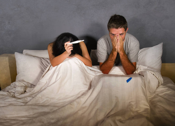 young couple in bed scared and stressed after positive result on pregnancy test with pregnant woman expecting unwanted baby and man feeling overwhelmed worried and disappointed  - Foto, imagen