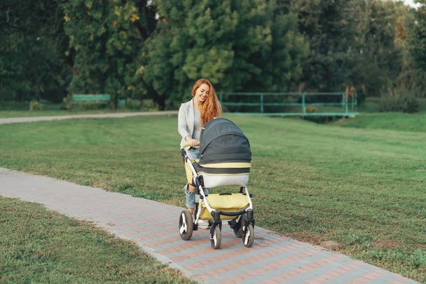 Een jonge moeder die genieten van het park lopen met haar kindje ontspannen zijn baby per kar. - Foto, afbeelding