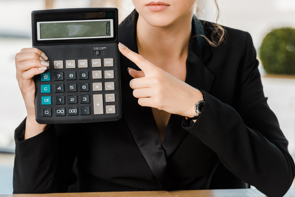 bijgesneden afbeelding van zakenvrouw wijzen op rekenmachine in kantoor - Foto, afbeelding