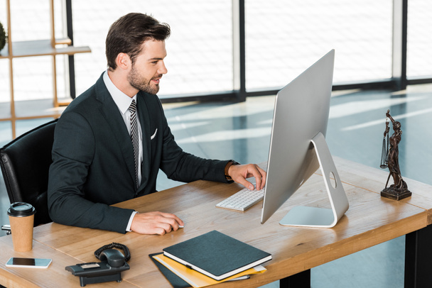 vista lateral del hombre de negocios guapo que trabaja con la computadora en la mesa en la oficina
 - Foto, Imagen
