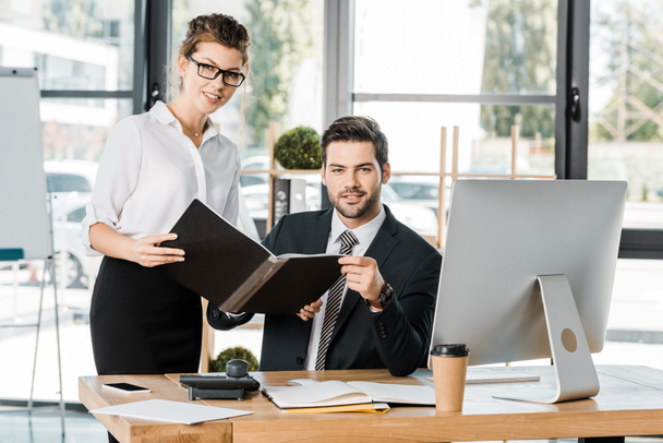 businesswoman and businessman holding folder with documents in office and looking at camera - Photo, Image